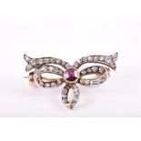 A diamond and garnet bow-shaped brooch the openwork mount inset with diamond accents, and centred