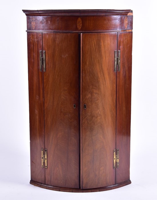 An Edwardian bow-fronted wall-hanging corner cupboard with double hinged central doors and
