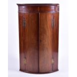 An Edwardian bow-fronted wall-hanging corner cupboard with double hinged central doors and