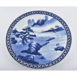 A 19th century Japanese Arita blue and white charger decorated with a mountainous river landscape,