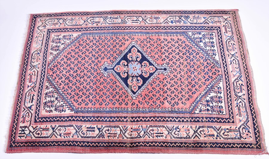 A Persian Qashqai carpet designed with central indigo diamond medallion against a salmon pink ground