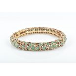An emerald hinged bangle of open-worked floral form, set throughout with round mixed-cut emeralds,