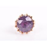 A yellow metal and synthetic corundum ring the mixed round-cut purple stone within a stylised yellow