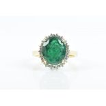 A diamond and emerald cluster ring set with a mixed oval-cut emerald surrounded with a border of