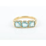 A yellow metal and blue gemstone ring collet-set with a round-cut stone flanked with square-cut