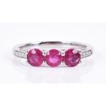 A platinum, diamond, and ruby ring set with three round-cut rubies, the shoulders inset with