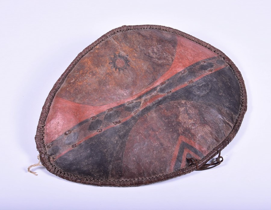 An early 20th century African leather shield of oval form with painted decoration, 79 cm x 58 cm.