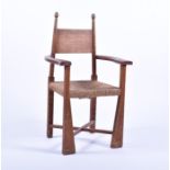 An Arts and Crafts oak child's rush seat elbow chair with cross stretcher, turned finials and curved