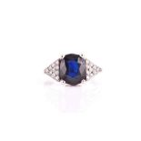 A 14ct white gold, diamond, and sapphire ring set with a cushion-cut dark blue sapphire, set each