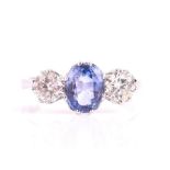 An 18ct white gold, diamond, and sapphire ring set with a mixed oval-cut pale blue sapphire, flanked