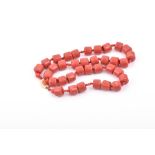 A coral-coloured necklace comprised of thirty five rounded beads carved from stone, fastened with