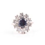 A white metal, diamond, and sapphire cluster ring set with a mixed oval-cut sapphire, surrounded