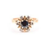 An 18ct yellow gold, diamond, and sapphire cluster ring centred with a round-cut dark blue sapphire,