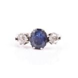 A platinum, diamond, and sapphire ring set with a mixed oval-cut sapphire, flanked with two old