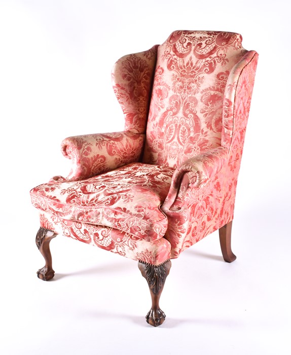 An English upholstered wingback armchair with pink rococo design fabric with studded metal detail to