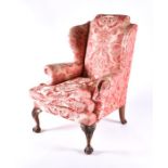 An English upholstered wingback armchair with pink rococo design fabric with studded metal detail to