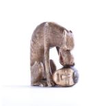 A 19th century Japanese ivory netsuke modelled as a wolf crouched over a severed human head,