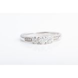 An 18ct white gold and diamond ring set with three round brilliant-cut diamonds, the shoulders inset