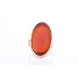 A yellow metal and carnelian ring set with an elongated oval carnelian plaque, within bezel mount,