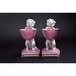 A pair of Brownfield posy vases modelled as dogs with a pink basket in their mouths, on a pink