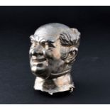 A cast white metal model of a male head possibly a politician or comedian, 9 cm high.