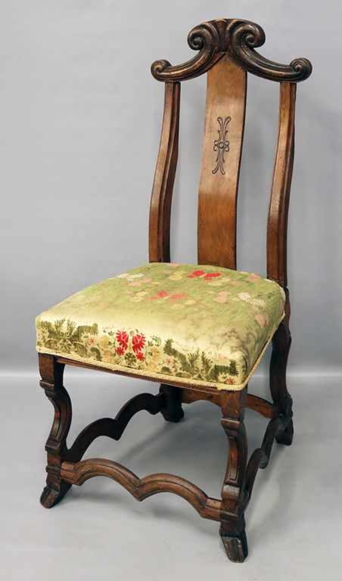 Barock-Stuhl.Hölzernes Gestell, reliefierte Rückenlehne mit Bekrönung, gepolsterte Sitzfläche.