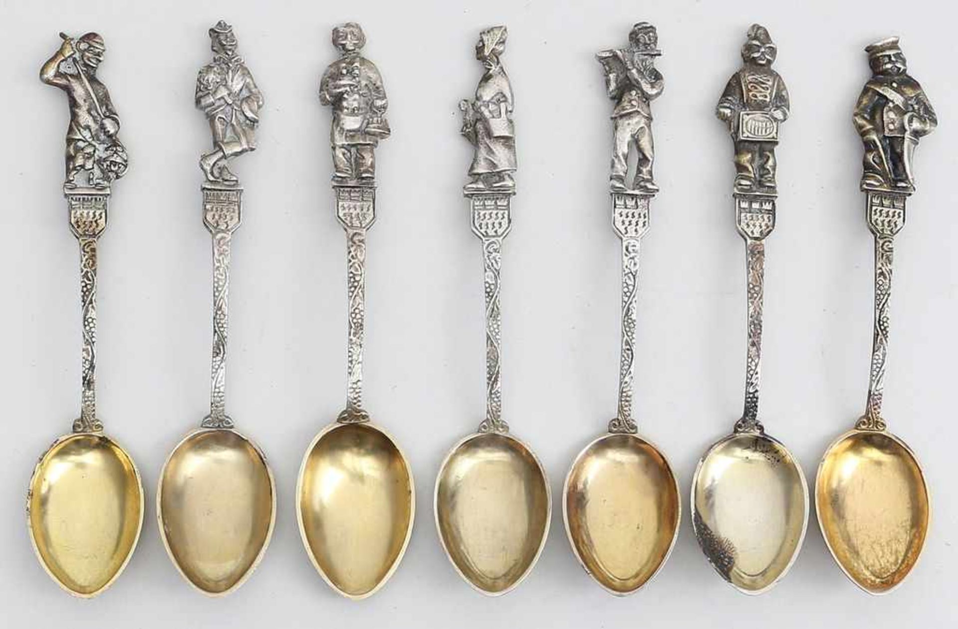 7 Mokkalöffel im Barockstil.800/000 Silber, 100 g. Figürliche Griffenden mit Figuren über Wappen,
