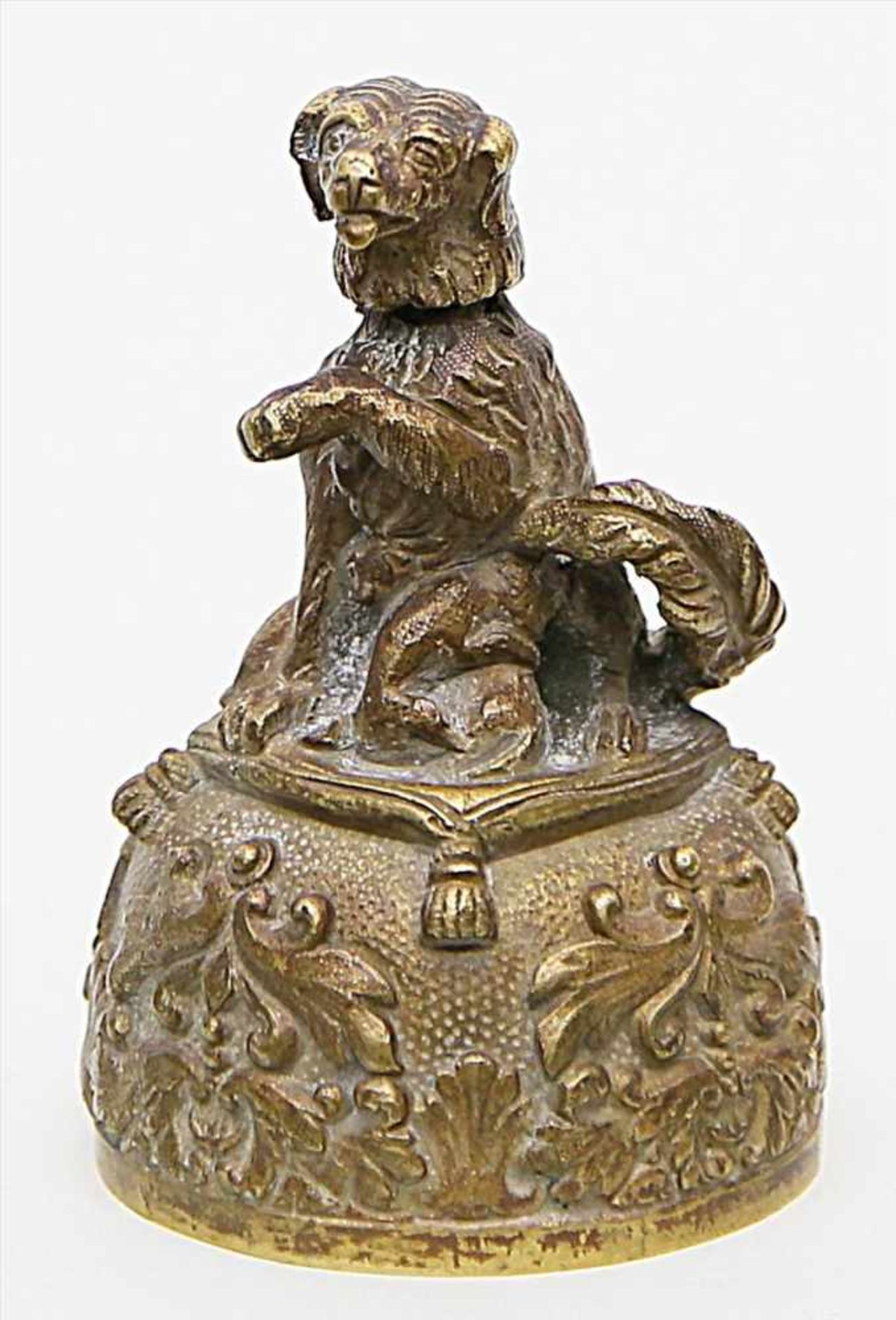 Figürliche Tischglocke.Bronze. Auf reich reliefierter Glocke sitzender, aufwartender Hund mit