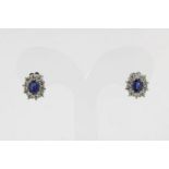 Witgouden entourage oorstekers bezet met briljant ca. 0.60ct. en blauwe saffier 0.92ct. , geh. 750/