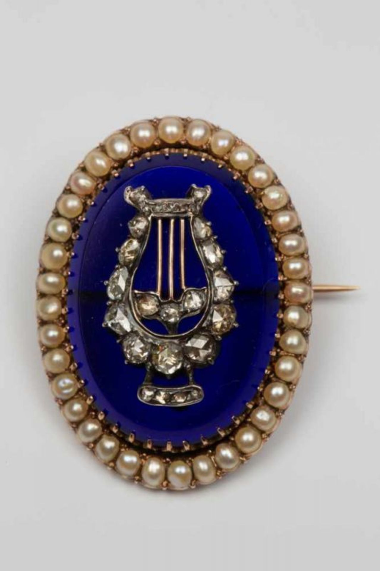 Roségouden ovale broche, begin 20e eeuw,gezet met blauw glas, waarop een zilveren lier, gezet met