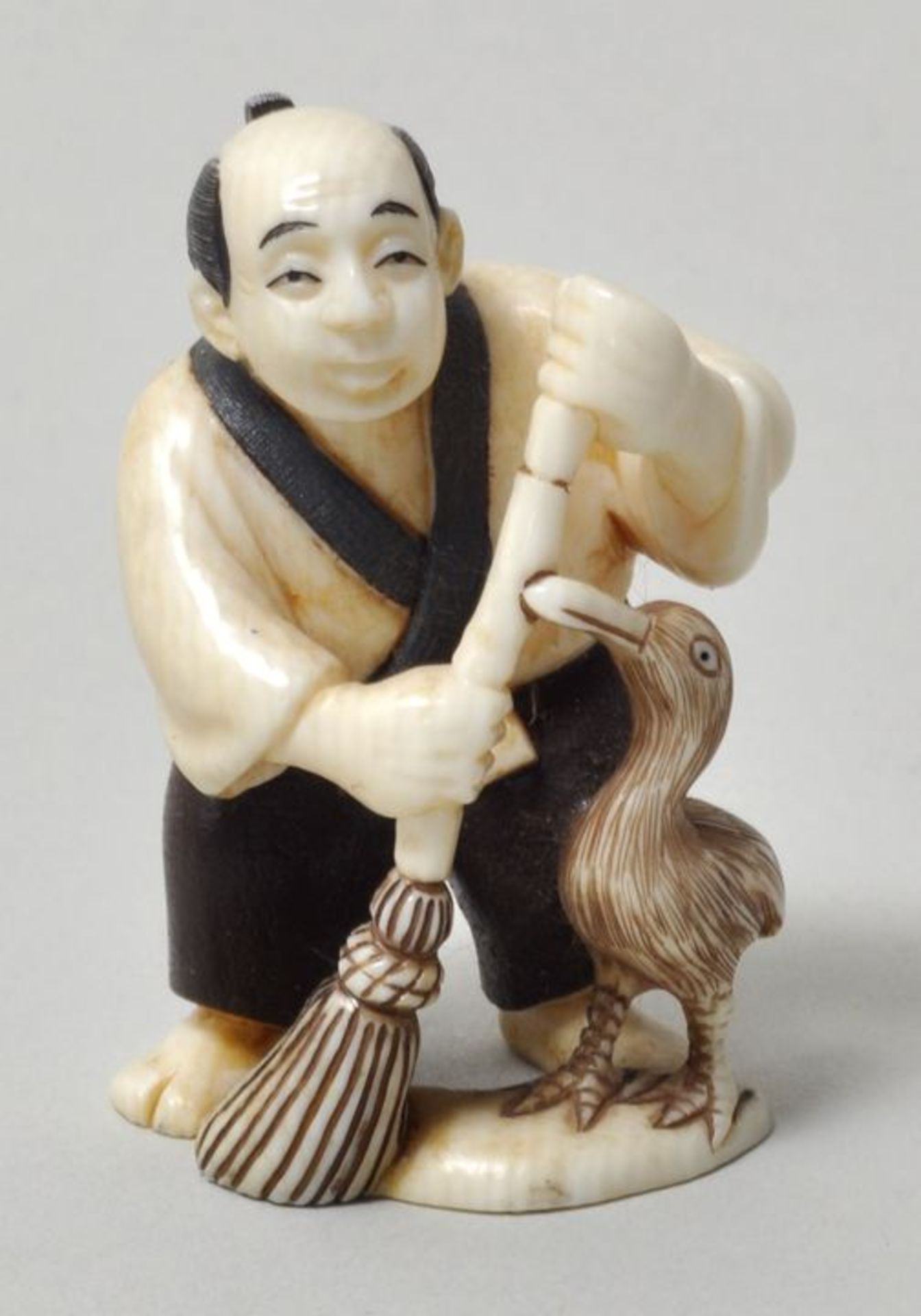 Netsuke, Japan, 20. Jh.Mann mit Besen und Kormoran. Elfenbein, geschnitzt, Details farbig, sign. (