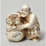 Netsuke, Japan, 19./ 20. Jh.Mann mit Okame-Maske (?). Elfenbein, geschnitzt, Binnengravur dreifarbig