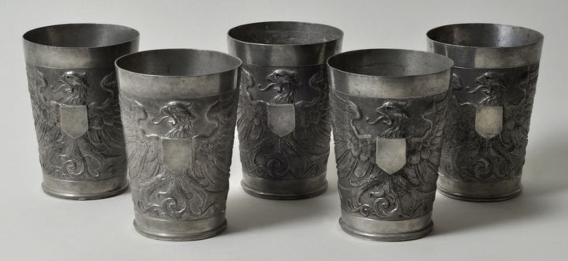 Fünf Becher, um 1890Zinn. Die konische Wandung reliefiert mit heraldischem Adler und vakanter