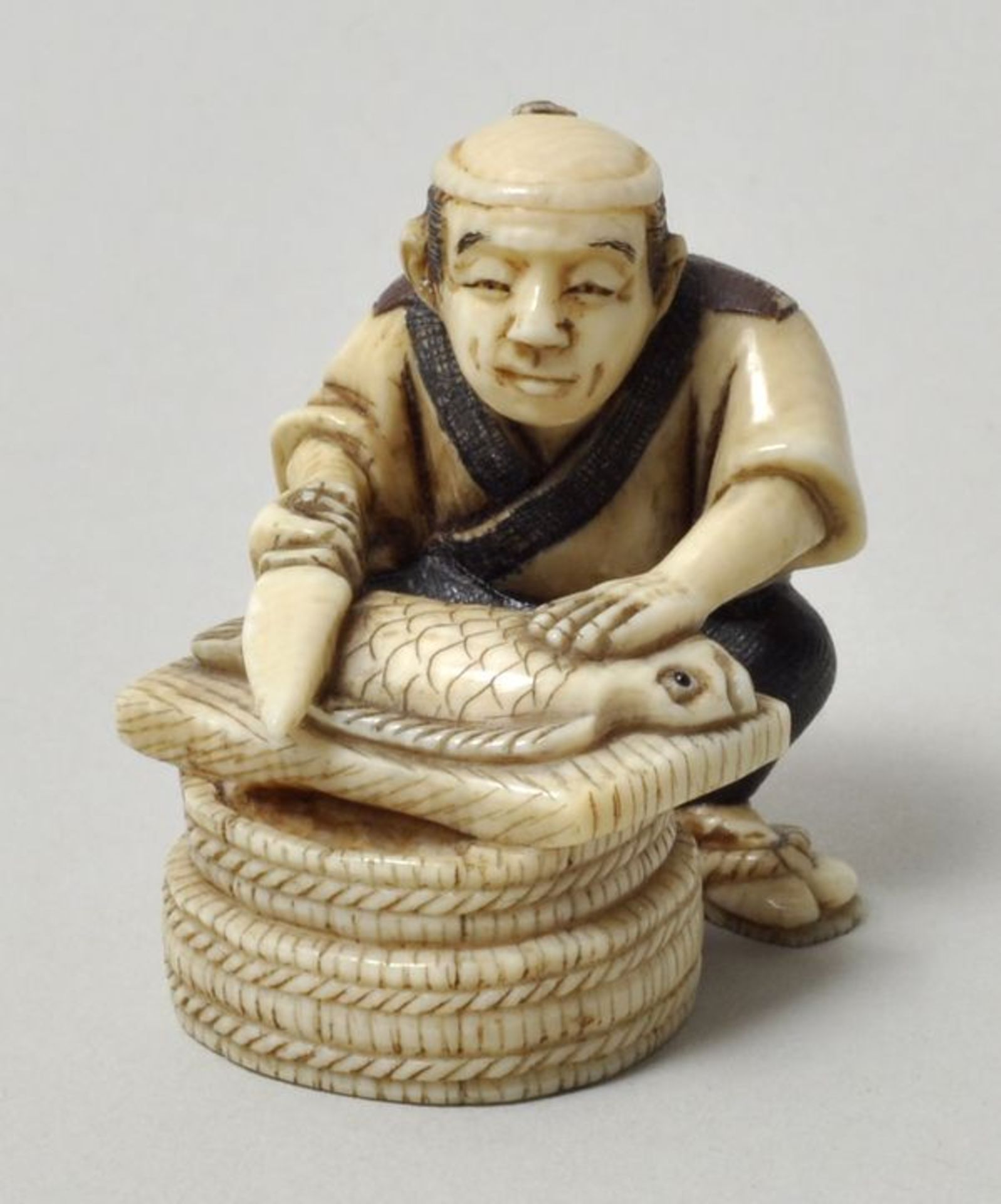 Netsuke, Japan, E. 19./ Anf. 20. JhElfenbein, geschnitzt, Details farbig. Mann beim Schuppen eines
