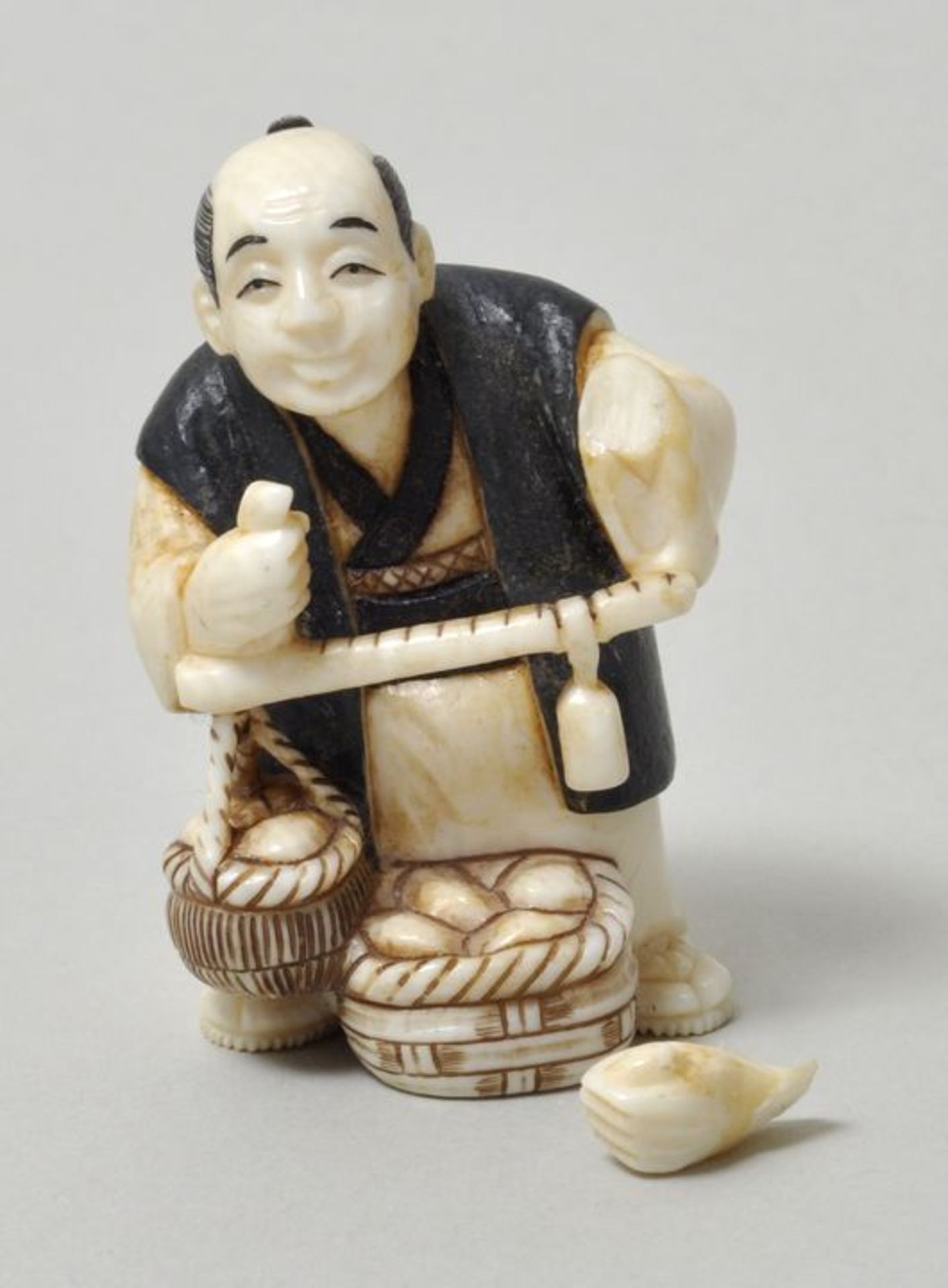 Netsuke, Japan, 19./ 20. Jh.Elfenbein, geschnitzt, schwarz und dunkelgrün bemalt: ein Händler mit