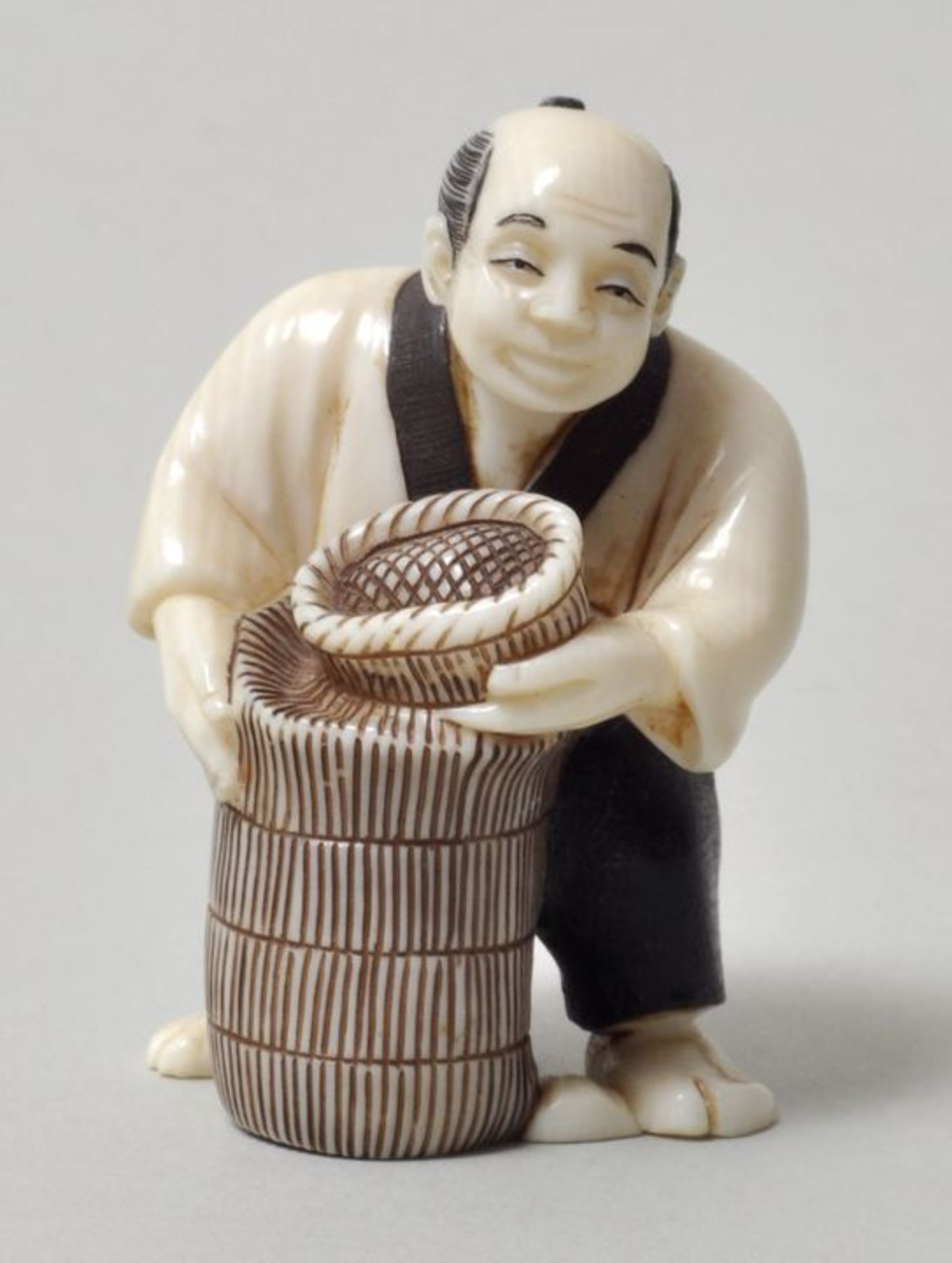 Netsuke, Japan, 20. Jh.Mann mit zwei Korbgefäßen. Elfenbein, geschnitzt, Details farbig, sign. (