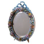 An English porcelain flower encrusted oval looking glass frame with wood easel stand, surmounted