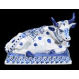 A Dutch Delft blue and white model of a recumbent cow, circa 1900, the underside with 'De Griekshe