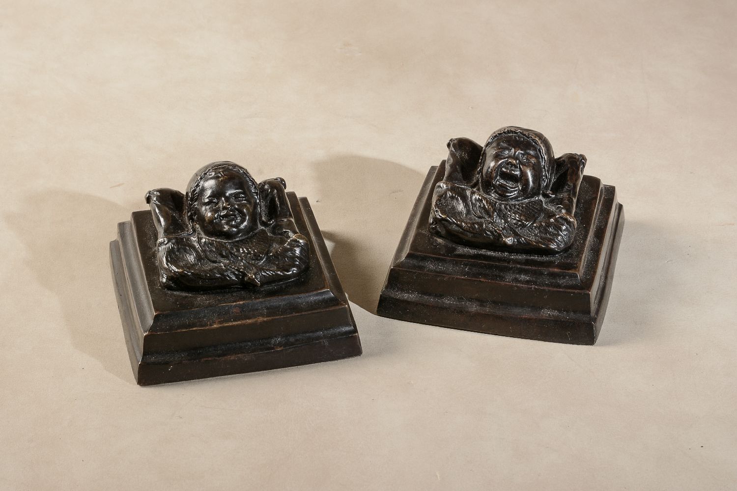 A pair of patinated bronze reliefs cast as infants' heads