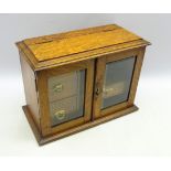Edwardian oak smokers cabinet, the glazed doors enclosing three fitted drawers,