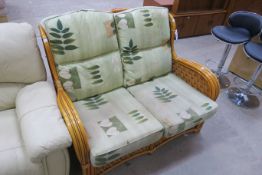 A Two Seater Cane Conservatory Settee with coloured fabric Cushions (est £20-£40). This lot is being