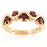 A GARNET DRESS RING in yellow gold, set with five round cut garnets in undulating form, British