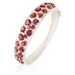 A GARNET BANGLE in sterling silver, set with round, pear, cushion and emerald cut garnets. 6cm inner