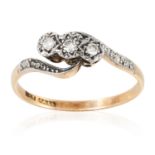 A THREE STONE DIAMOND RING in yellow gold, set with three round cut diamonds in scrolling design,