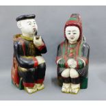 Pair of wooden painted male and female figures, each modelled seated with a basket on their backs,