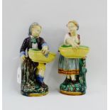 A pair of Minton Majolica boy and girl figures, each modelled standing and holding a basket,