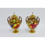 A pair of Royal Worcester floral study lidded urn vases, each with gilded handles and painted with