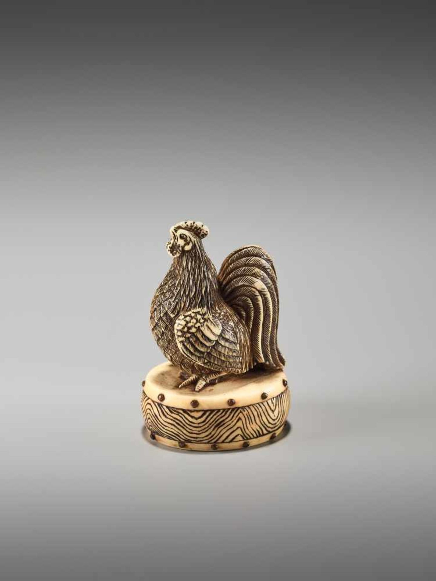 A FINE NETSUKE OF A COCKEREL ON A DRUM BY KOJITSU By Kojitsu, ivory netsuke with horn inlayJapan,