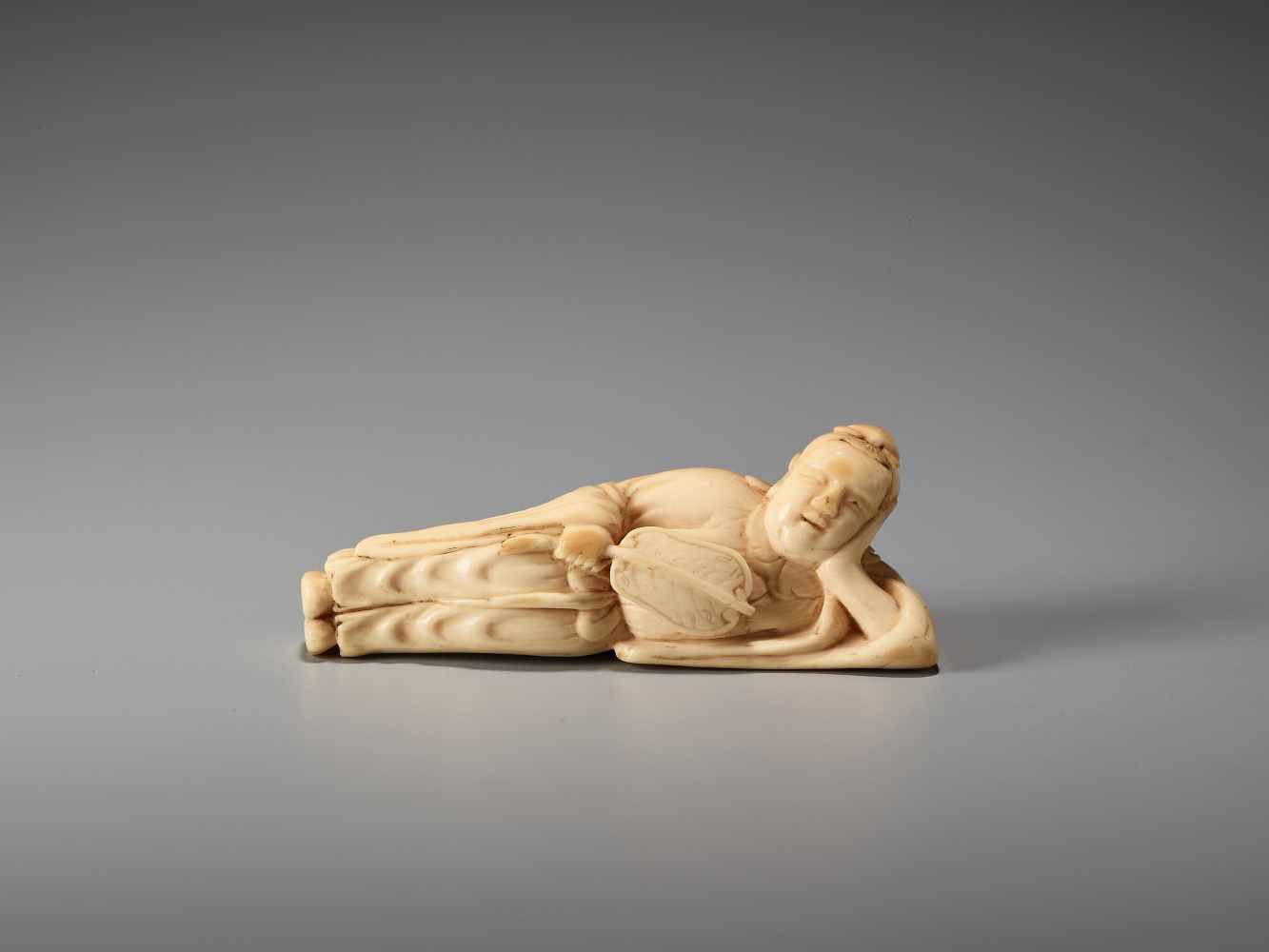 AN IVORY NETSUKE OF A RECLINING CHINESE IMMORTAL WITH A FANUnsigned, ivory netsukeJapan, late 18th - Image 3 of 6