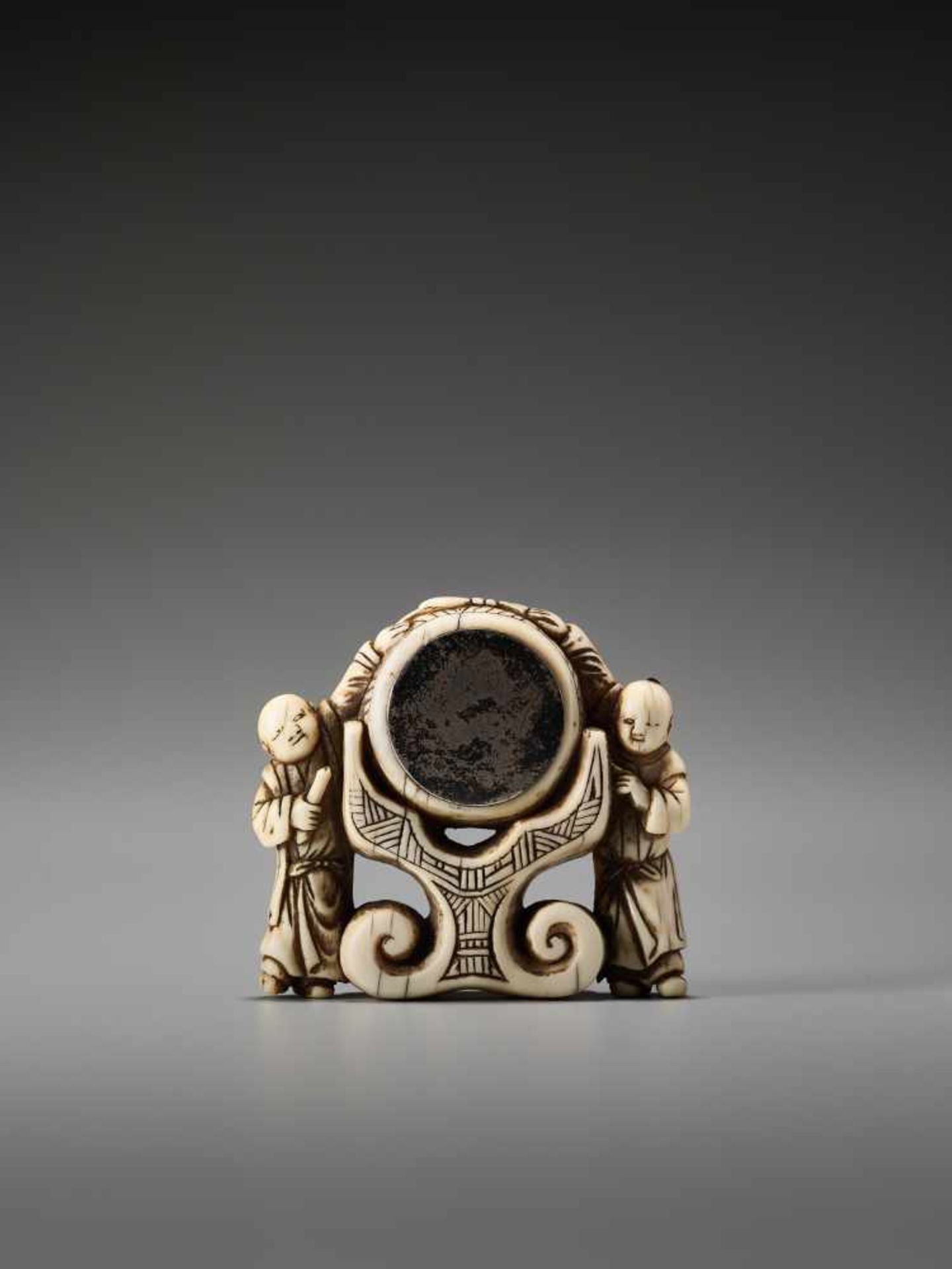 A RARE AND UNUSUAL IVORY NETSUKE OF TWO CHINESE BOYS AT A PALACE GONGUnsigned, ivory netsuke with